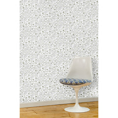  A white swivel chair in front of a wall papered in a large-scale minimal floral print in shades of tan and gray on a white background.