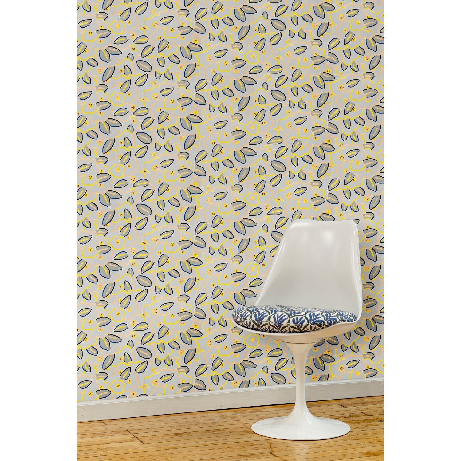  A white swivel chair in front of a wall papered in a large-scale minimal floral print in shades of navy, yellow and pink on a gray-blue background.