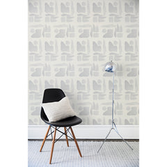 A chair and floor lamp in front of a wall papered in a large-scale pattern of abstract gray watercolor shapes on a cream background.