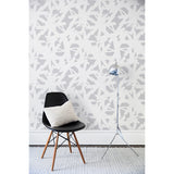 Chair and floor lamp in front of a wall papered in a bold white brushtroke pattern on a light gray background.