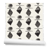 Partially unrolledwallpaper in a large-scale pattern of black watercolored diamonds, circles and lines on a cream background. 