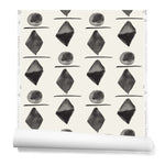 Partially unrolledwallpaper in a large-scale pattern of black watercolored diamonds, circles and lines on a cream background. 