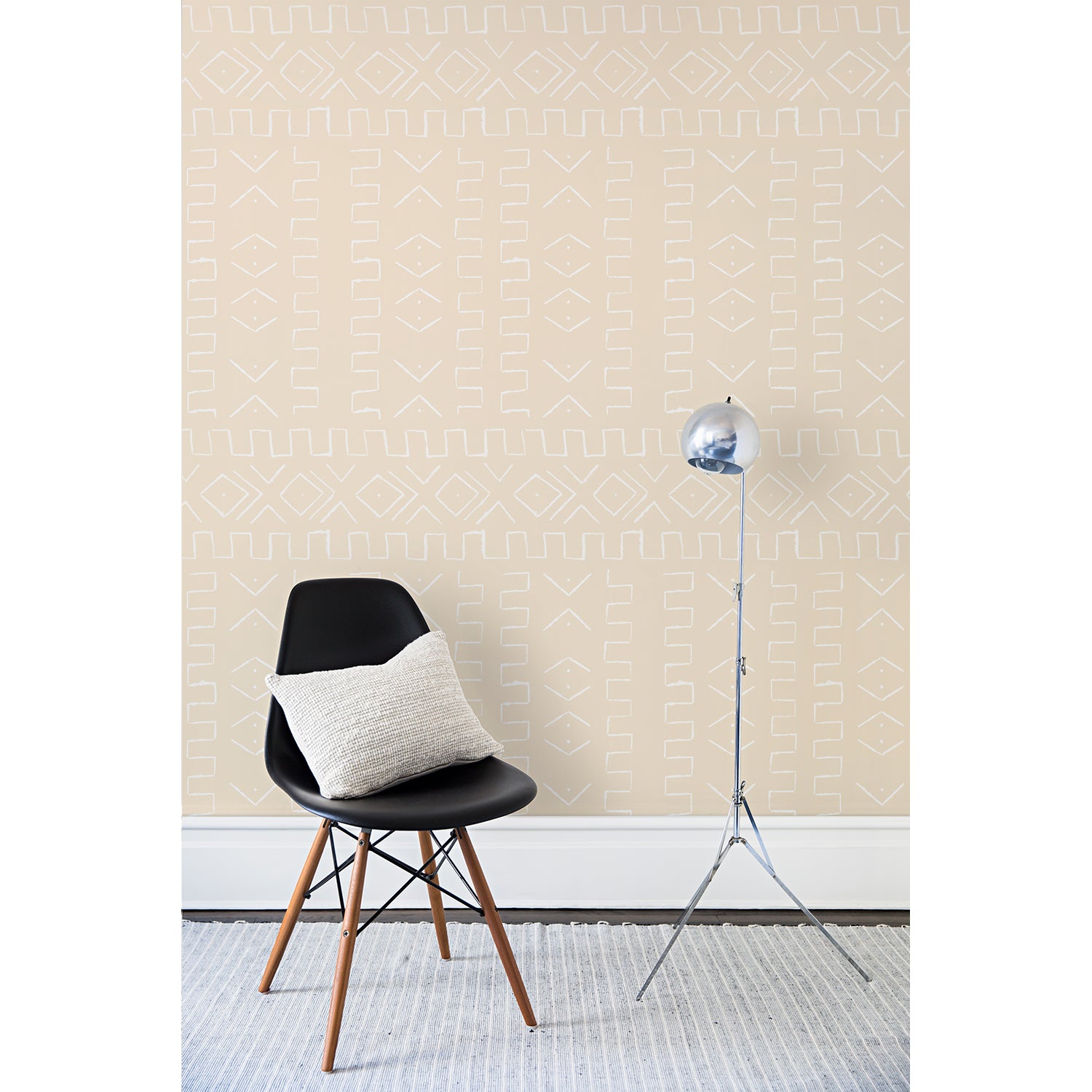 A chair and floor lamp in front of a wall papered in a minimalist African-inspired line design of painted white on a beige background.