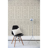 A chair and floor lamp in front of a wall papered in a minimalist African-inspired line design of painted gray on a beige background.