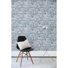 A chair and floor lamp in front of a wall papered in a dense hand-drawn geometric motif in shades of navy on a white background.