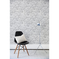 A chair and floor lamp in front of a wall papered in a dense hand-drawn geometric motif in shades of gray on a white background.