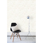 A chair and floor lamp in front of a wall papered in a dense hand-drawn geometric motif in shades of tan on a white background.