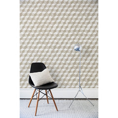 A chair and floor lamp in front of a wall papered in a hand-painted tumbling block pattern in shades of beige on a white background.