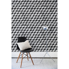 A chair and floor lamp in front of a wall papered in a hand-painted tumbling block pattern in black and gray on a white background.