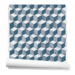 Partially unrolled wallpaper in a hand-painted tumbling block pattern in shades of blue on a white background.