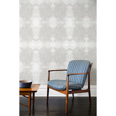 A wooden chair and coffee table in front of a wall papered in a dense hand-drawn symmetrical pattern in shades of gray on a white background.