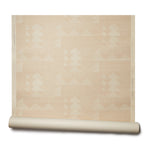 Partially unrolled wallpaper roll with layered geometric shapes in cream printed on a sandy tan background.