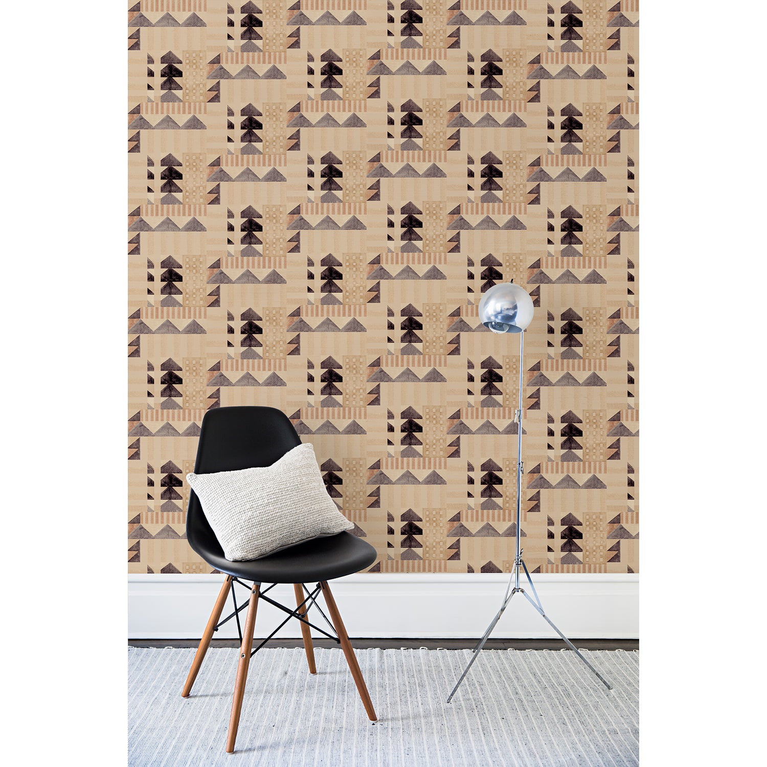 Partially unrolled wallpaper roll with layered geometric shapes in shades of black, beige and rust printed on a tan background.