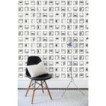 A chair and floor lamp in front of a wall papered in rows of block-printed black moons in various phases on a white background.