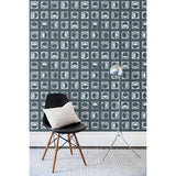 A chair and floor lamp in front of a wall papered in rows of block-printed white moons in various phases on a charcoal background.
