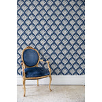 An antique chair in front of a wall papered in a repeating Moroccan-inspired scallop pattern in navy and white on a blue background.