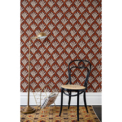A chair and floor lamp in front of a wall papered in a repeating Moroccan-inspired scallop pattern in white and red on a maroon background.