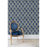 An antique chair in front of a wall papered in a repeating Moroccan-inspired scallop pattern in navy and green on a white background.