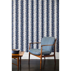 An armchair and coffee table in front of a wall papered in repeating horizontal stripes of black and blue branches and fruit on a white background.