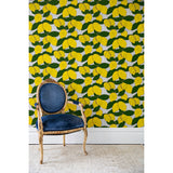A blue armchair in front of a wall papered in a large-scale painted lemon and leaf print in yellow and green on a light blue background.