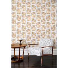 An armchair and side table in front of a wall papered in a large-scale cartoon seaweed print in bronze on a white background.
