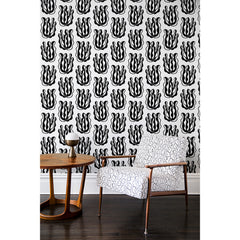 An armchair and side table in front of a wall papered in a large-scale cartoon seaweed print in black on a white background.