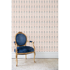 An antique chair in front of a wall papered in repeating rows of a watercolor flowers in tan and gray on a light pink background.