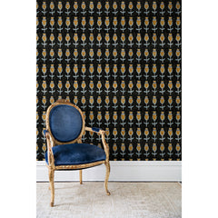 An antique chair in front of a wall papered in repeating rows of a watercolor flowers in gray, mustard and light blue on a black background.