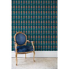 An antique chair in front of a wall papered in repeating rows of a watercolor flowers in red, gray and blue on a turquoise background.