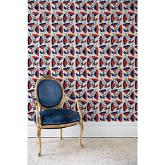 An antique chair in front of a wall papered in a repeating pattern of large-scale graphic flowers in red and navy on a cream background.