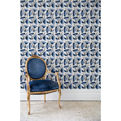An antique chair in front of a wall papered in a repeating pattern of large-scale graphic flowers in shades of blue on a cream background.