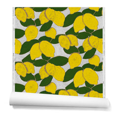 A hanging roll of wallpaper with a large-scale painted lemon and leaf print in yellow and green on a light blue background.