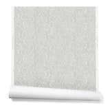 A hanging roll of wallpaper with a large-scale repeating leaf print in white on a light gray watercolor background.