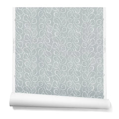 A hanging roll of wallpaper with a large-scale repeating leaf print in white on a blue-gray watercolor background.