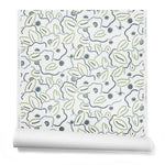 A hanging roll of wallpaper in a large-scale minimal floral print in shades of navy, blue-gray and green on a white background.