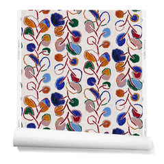A hanging roll of wallpaper with repeating rows of colorful leaf prints in shades of red, purple and blue on a cream background.