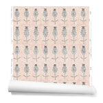 A hanging roll of wallpaper with repeating rows of a watercolor flowers in tan and gray on a light pink background.
